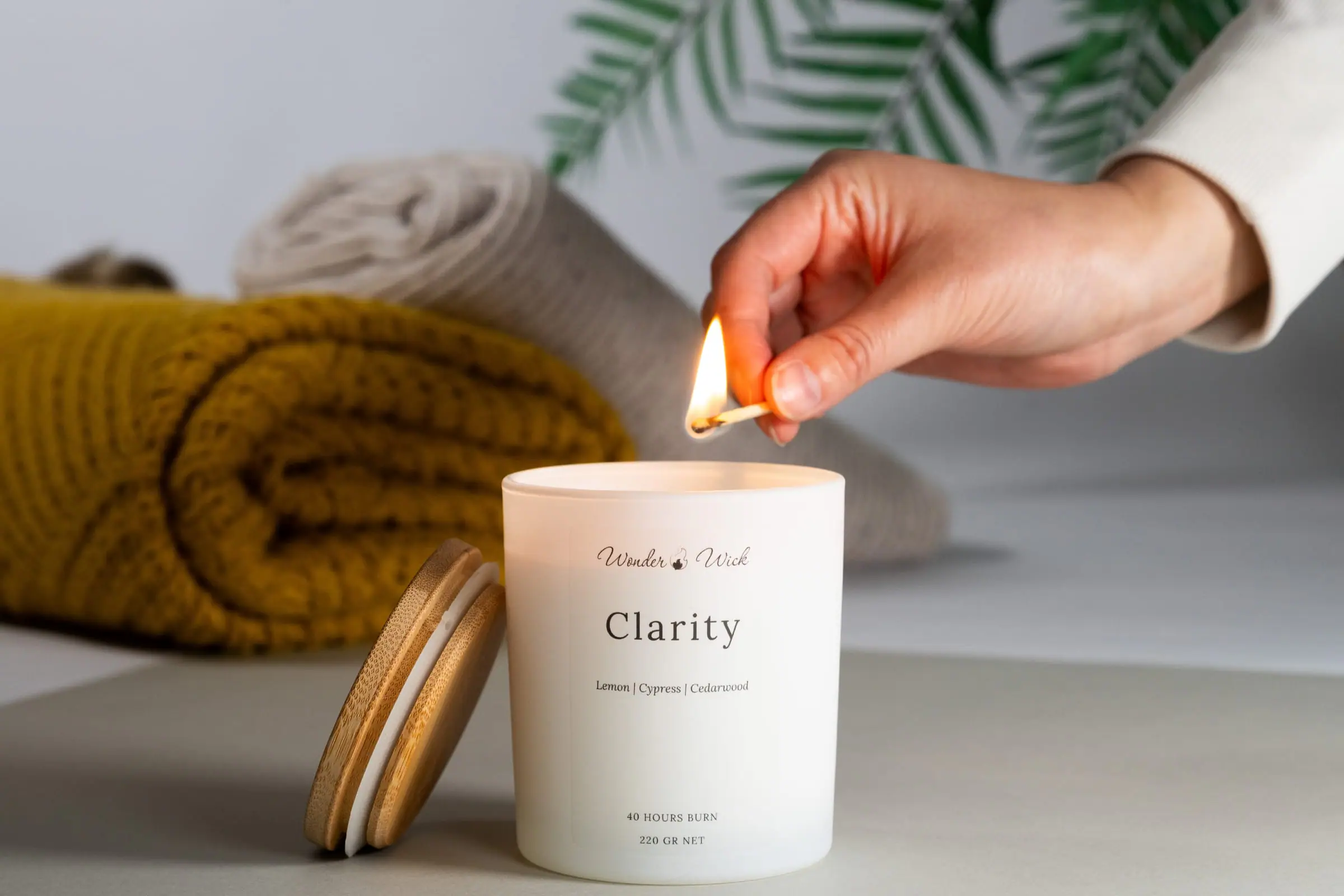 A hand lighting the Clarity aromatherapy candle beside its wooden lid