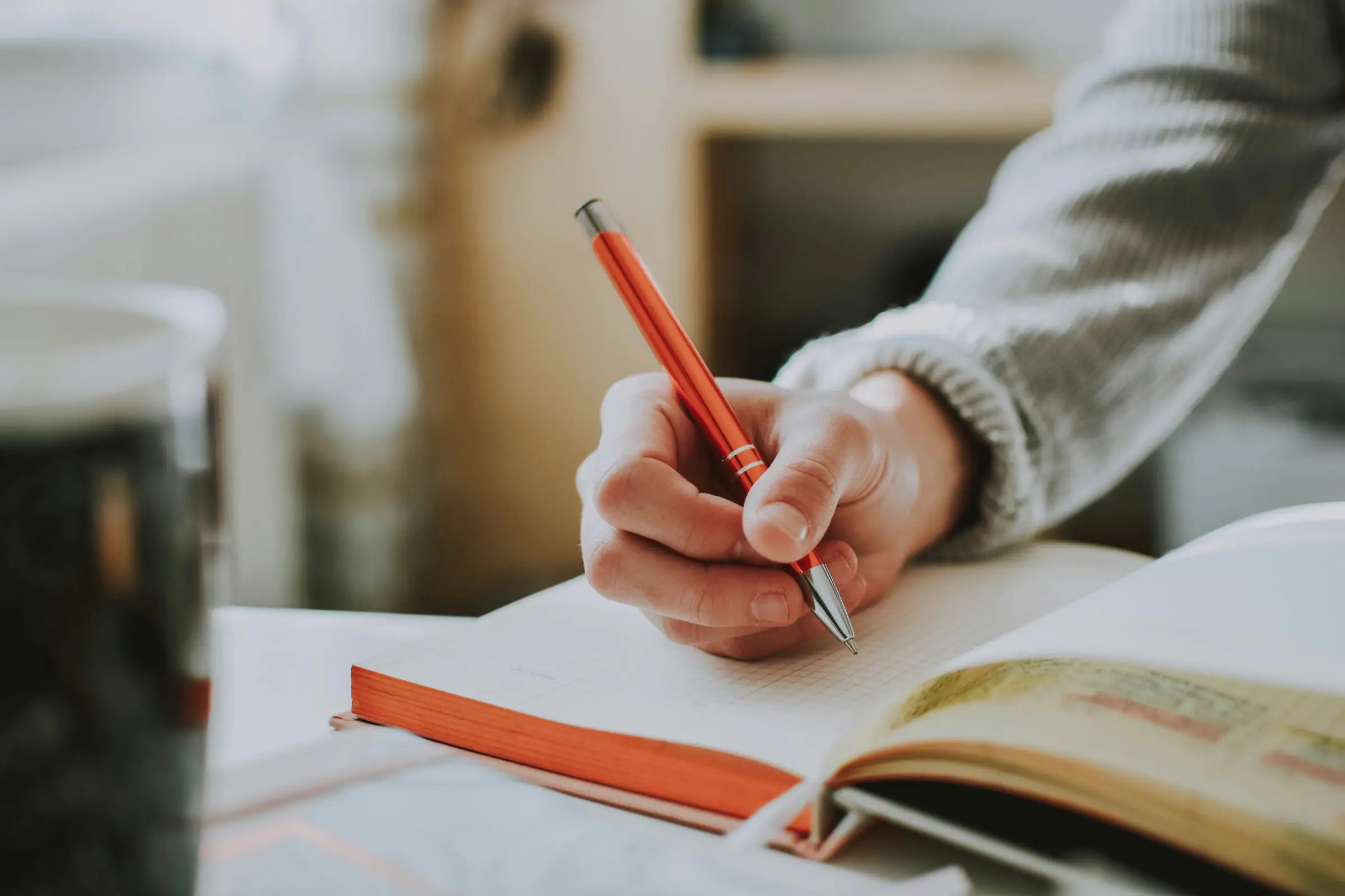 Hand writing in a notebook with a red pencil at a bright workspace